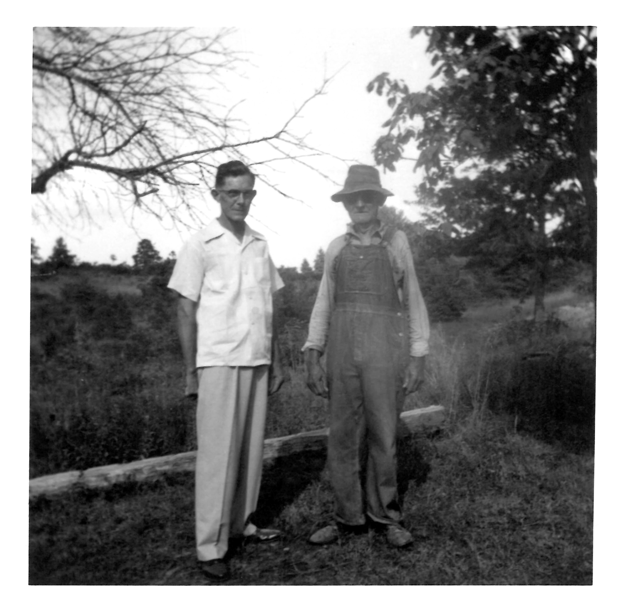 Black and white photo of Colonel's dad and grandfather standing in a field next to trees