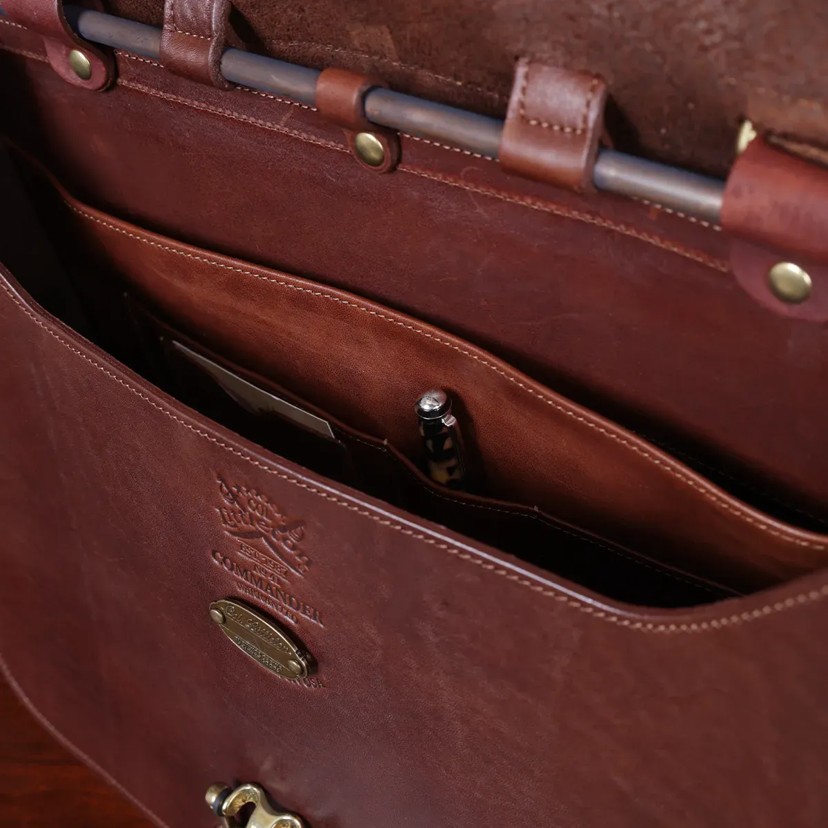 commander leather laptop briefcase on a wooden table with a dark background - inside view of pockets with pen and business card