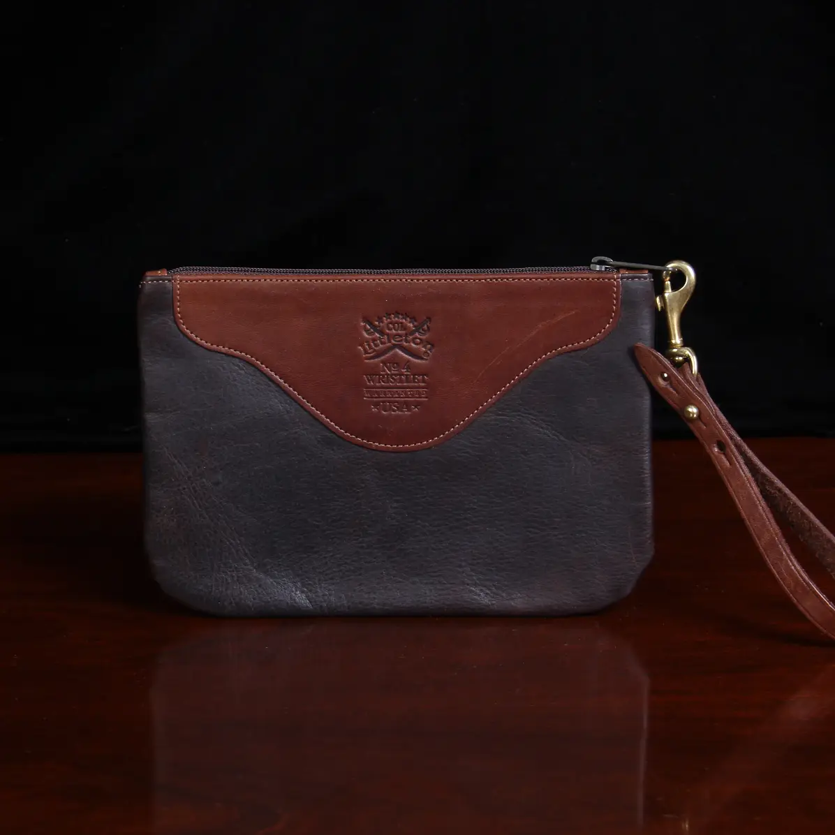 back view brown leather wristlet clutch on black background and wood table