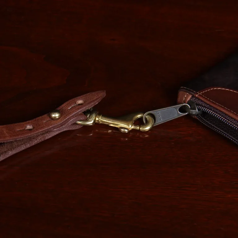 closeup view of clasp and zipper of brown leather wristlet clutch on black background and wood table