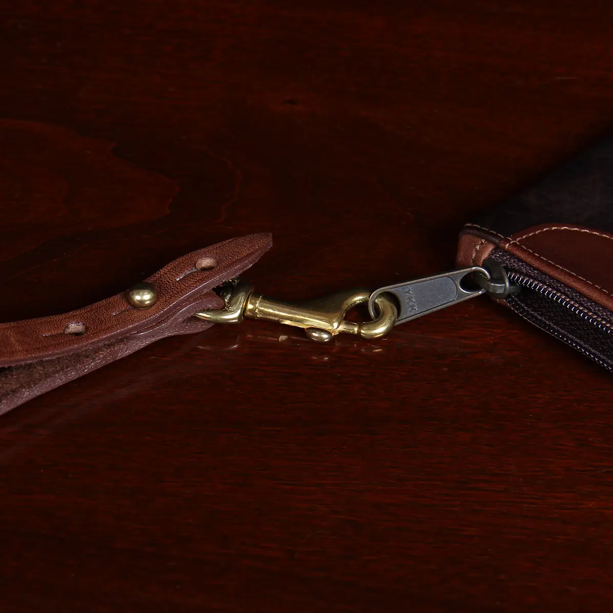 closeup view of clasp and zipper of brown leather wristlet clutch on black background and wood table