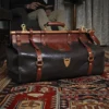 Dark brown buffalo leather No. 3 grip travel bag sitting on an antique carpet with a man reading in a chair in the background