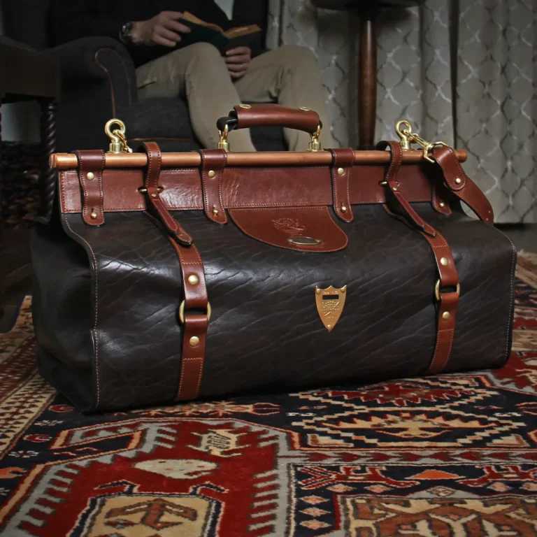 Dark brown buffalo leather No. 3 grip travel bag sitting on an antique carpet with a man reading in a chair in the background