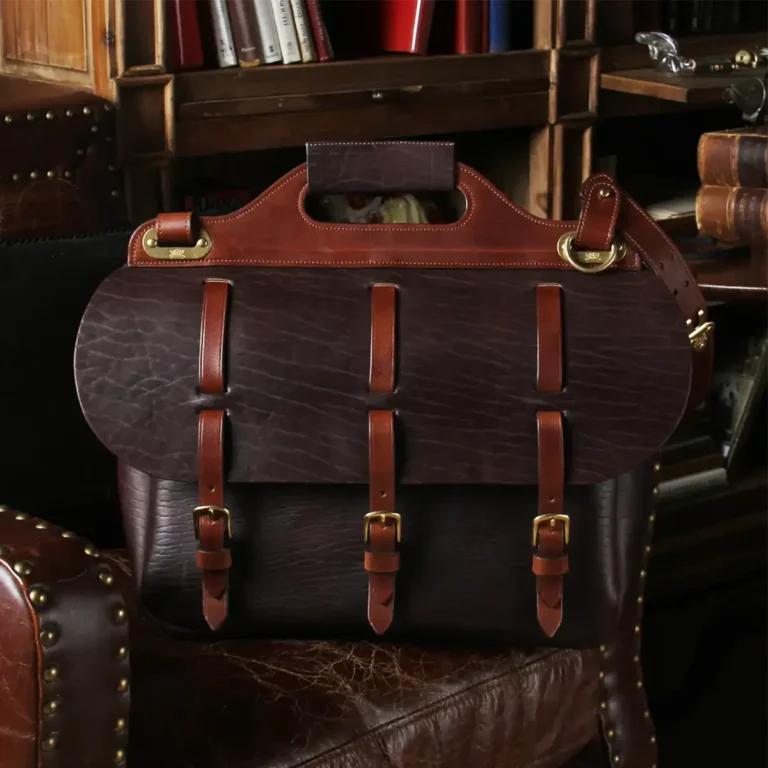 Military-inspired, dark brown American Buffalo leather No. 1 Saddlebag Briefcase on antique leather chair in a darkly lit study