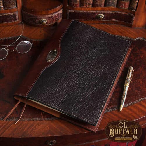 Dark drown buffalo leather composition journal cover on small antique desk with spectacles and antique pen beside it