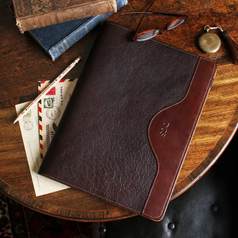 no 28 leather portfolio in tobacco buffalo on a table with glasses, books, pencil, paper, and pocket watch