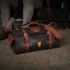 No. 2 Duffel Bag in Tobacco Brown American Buffalo with Vintage Brown American Steerhide trim - Front view of back resting on the floor next to a man tying his shoe in an antique chair