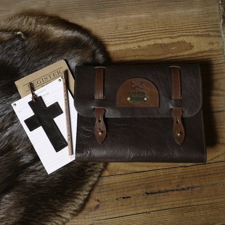 Leather Bible cover on wood surface with journal, pencil, and cross bookmark