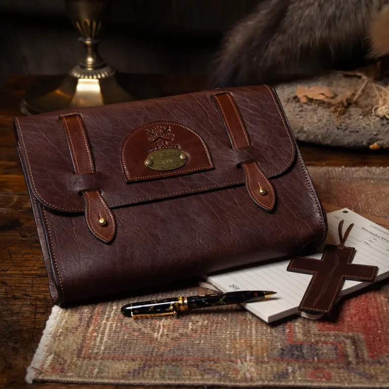 front view of closed leather bible cover pocket with pen, notepad, cross bookmark, and journal on wooden desk