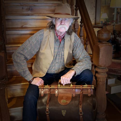 Colonel sitting on steps, holding Tobacco Brown American Buffalo No. 3 Grip Bag, looking directly at viewer