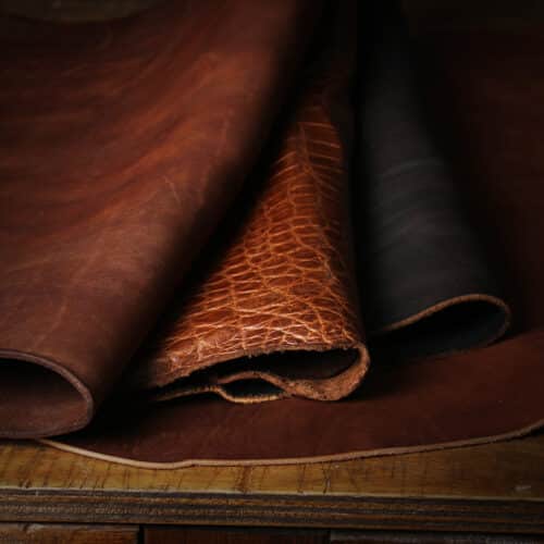 Three kinds of full-grain leather hides overlapping. In order left to right: Vintage Brown American Steerhide, Brown American Alligator, and Tobacco Brown American Buffalo