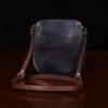 back view of a dark brown leather Bella Bag small crossbody with boot on front made from alligator hide sitting on a wood table and black background