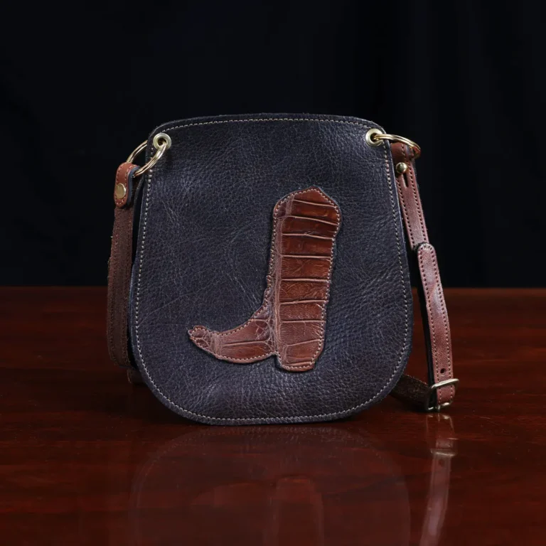 dark brown leather Bella Bag small crossbody with boot on front made from alligator hide sitting on a wood table and black background