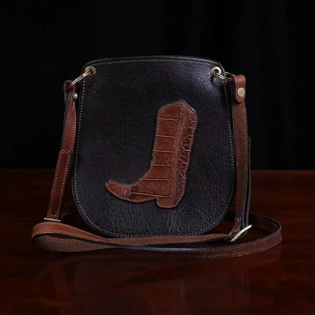 dark brown leather Bella Bag small crossbody with boot on front made from alligator hide sitting on a wood table and black background