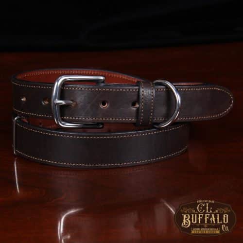 dark brown leather belt with nickel hardware coiled up on wood table