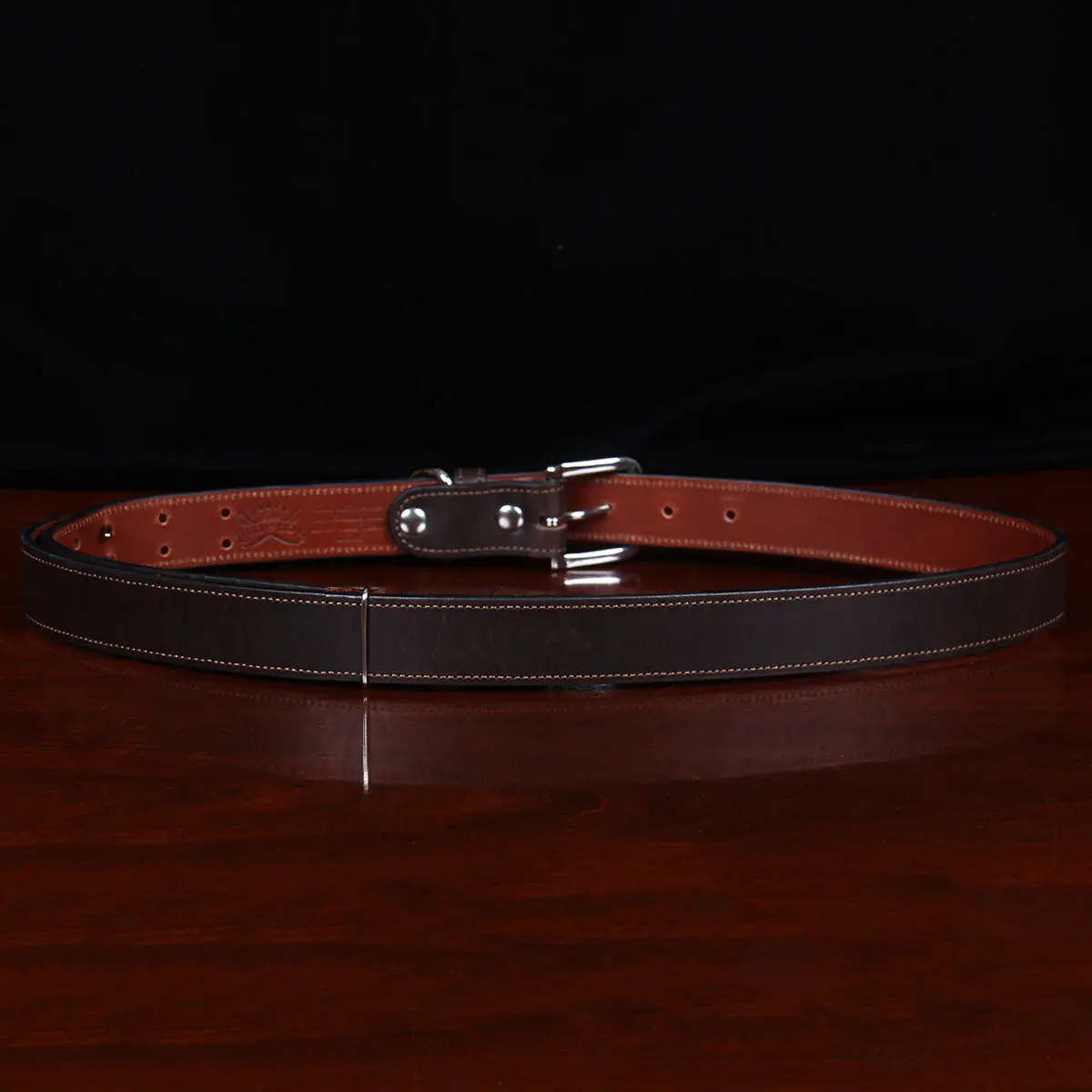 back view dark brown leather belt with nickel hardware on wood table