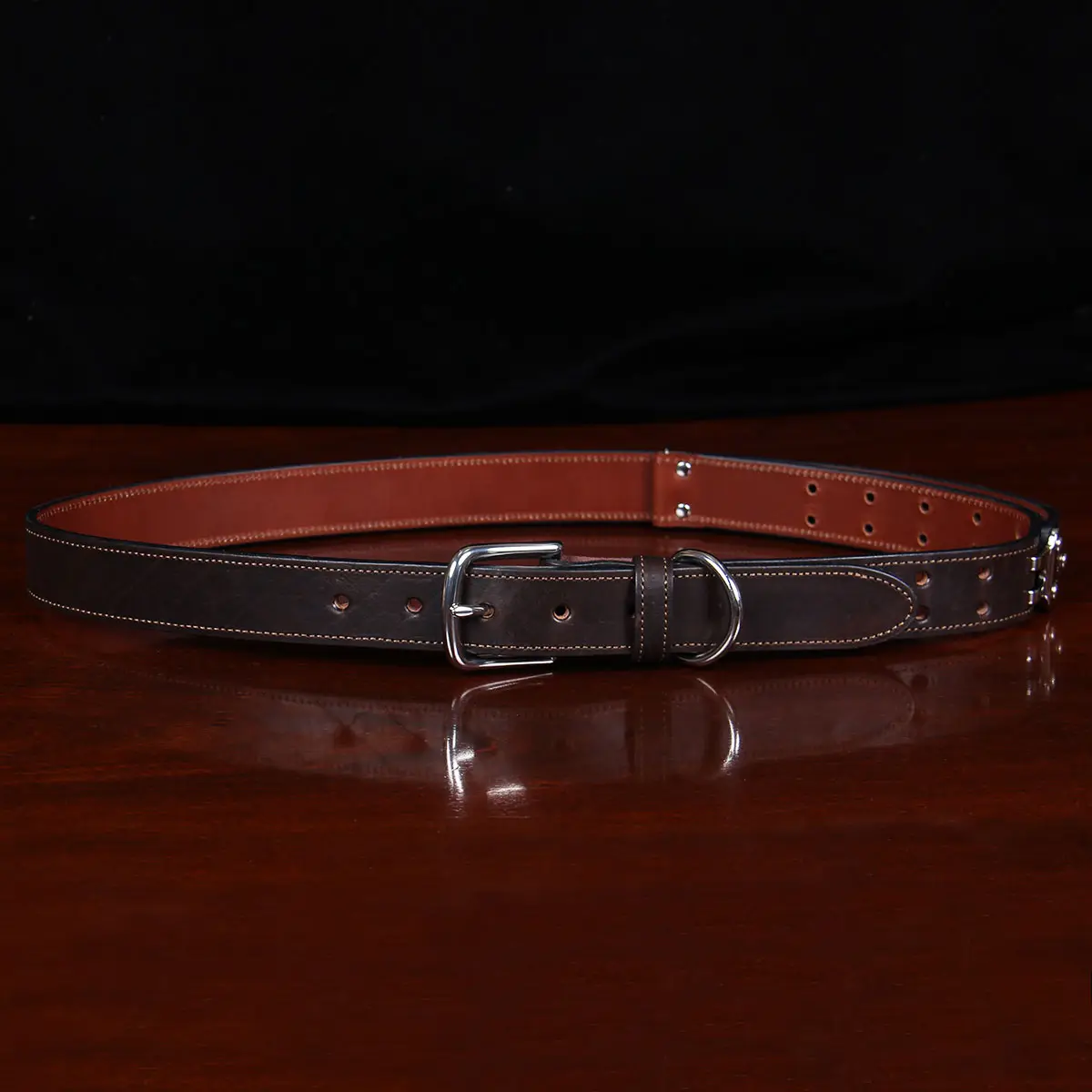front view dark brown leather belt with nickel hardware on wood table