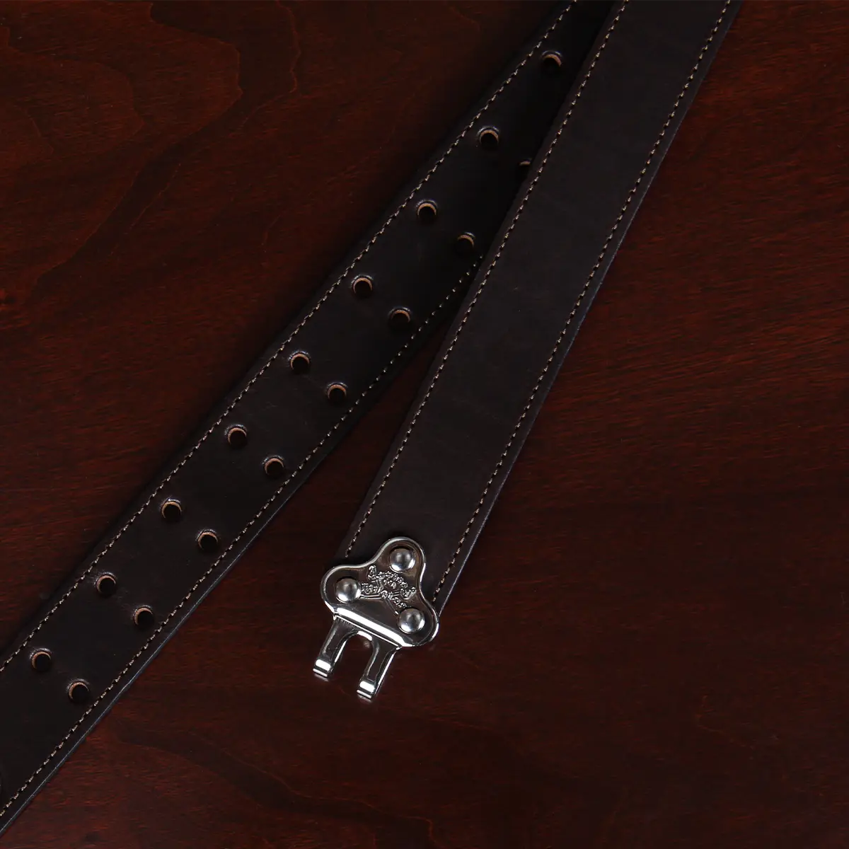 close-up view dark brown leather belt with nickel hardware on wood table