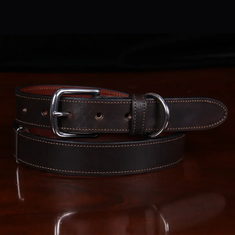 dark brown leather belt with nickel hardware coiled up on wood table