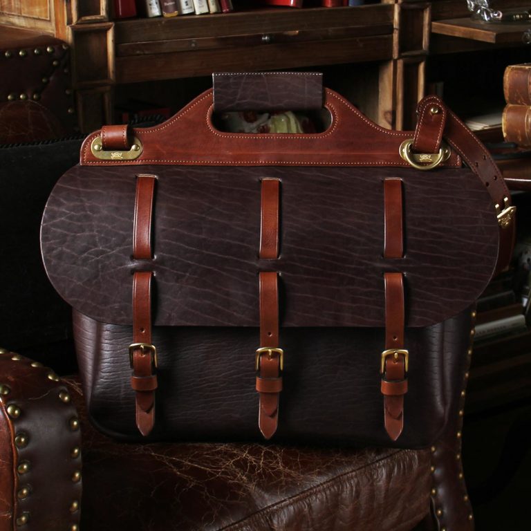 Military-inspired, dark brown American Buffalo leather No. 1 Saddlebag Briefcase on antique leather chair in a darkly lit study