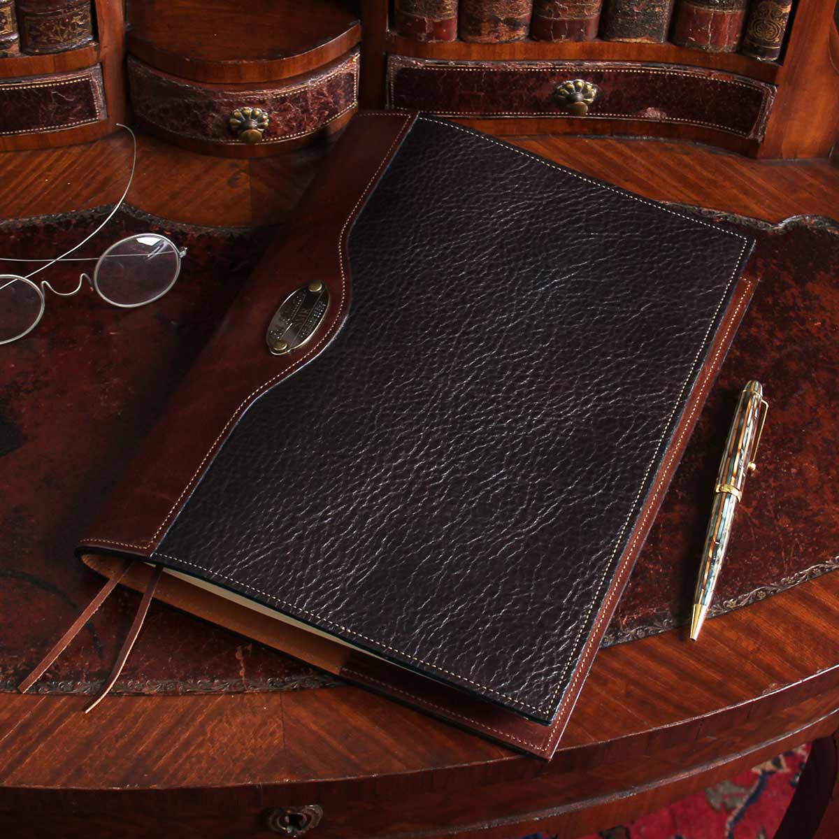 Dark drown buffalo leather composition journal cover on small antique desk with spectacles and antique pen beside it