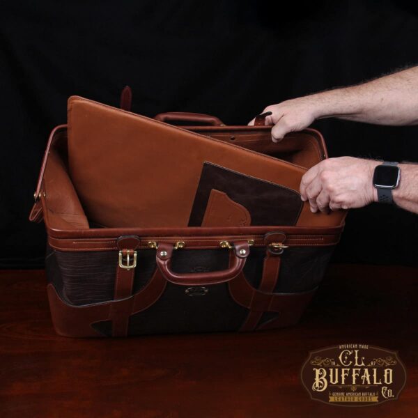 Vintage-style Gladstone dark brown american buffalo leather No. 5 Grip travel bag on wooden table - man pulling out removable bottom panel with secret pocket