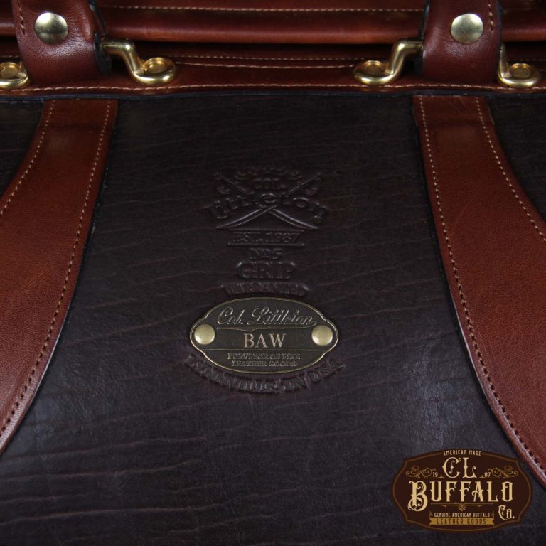 Vintage-style Gladstone dark brown american buffalo leather No. 5 Grip travel bag on wooden table - detail view of logo stamp and personalization plate