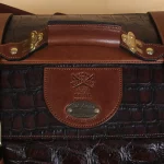 close-up view of grip handle of brown american alligator duffel bag on cream background