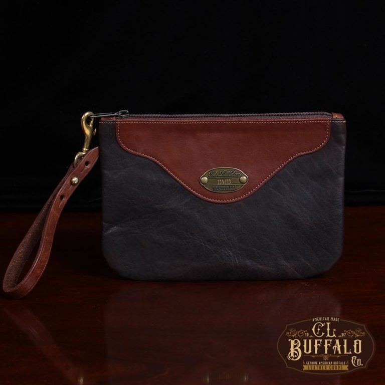front view brown leather wristlet clutch on black background and wood table