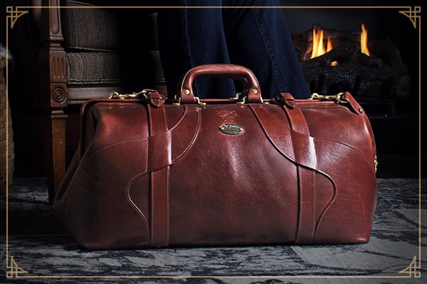 No. 5 Grip Travel Bag in Vintage Brown American Steerhide resting on an elegant rug in front of a lit fireplace