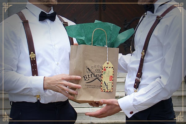 Two men wearing white dress shirts and No. 2 Col. Littleton Suspenders exchanging a small Col. Littleton Gift bag