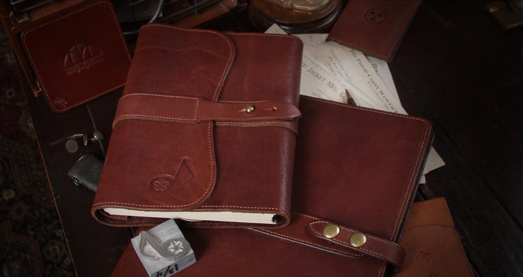 A No. 9 Journal and No. 18 Portfolio on a desk with logos stamped on each. A metal embossing stamp is next to them.