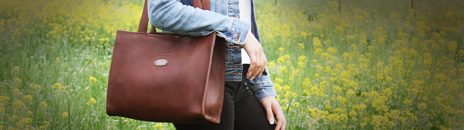 Leather Handbags Category Header - Vintage Brown Wayfarer Tote over woman's shoulder standing in field of yellow flowers