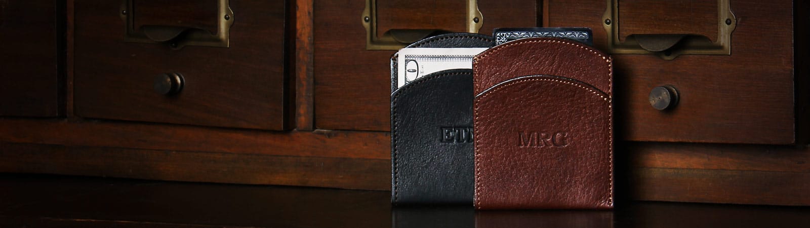 Wallets and Key Rings Category Header - Two leather Front Pocket Wallets in a wooden shelf, vintage brown in the front and black in the back