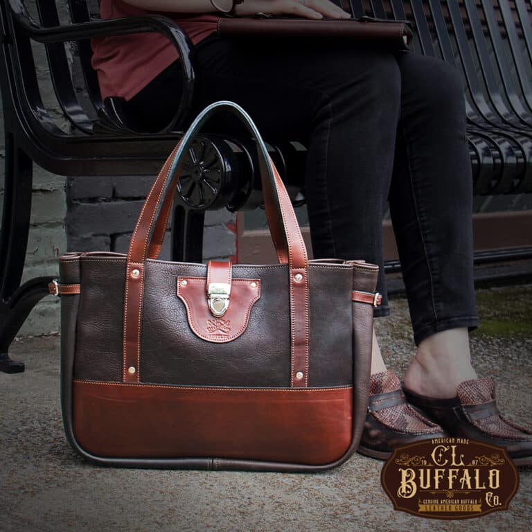 Bentley Tote in dark Tobacco Brown American Buffalo with contrasting vintage brown American Steerhide Trim on the ground next to a woman sitting on a black metal bench