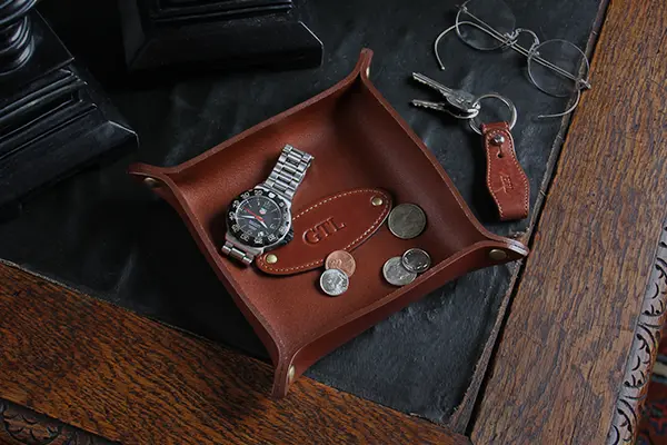 leather dresser caddy with coins and a watch sitting in it with a key chain on the left side