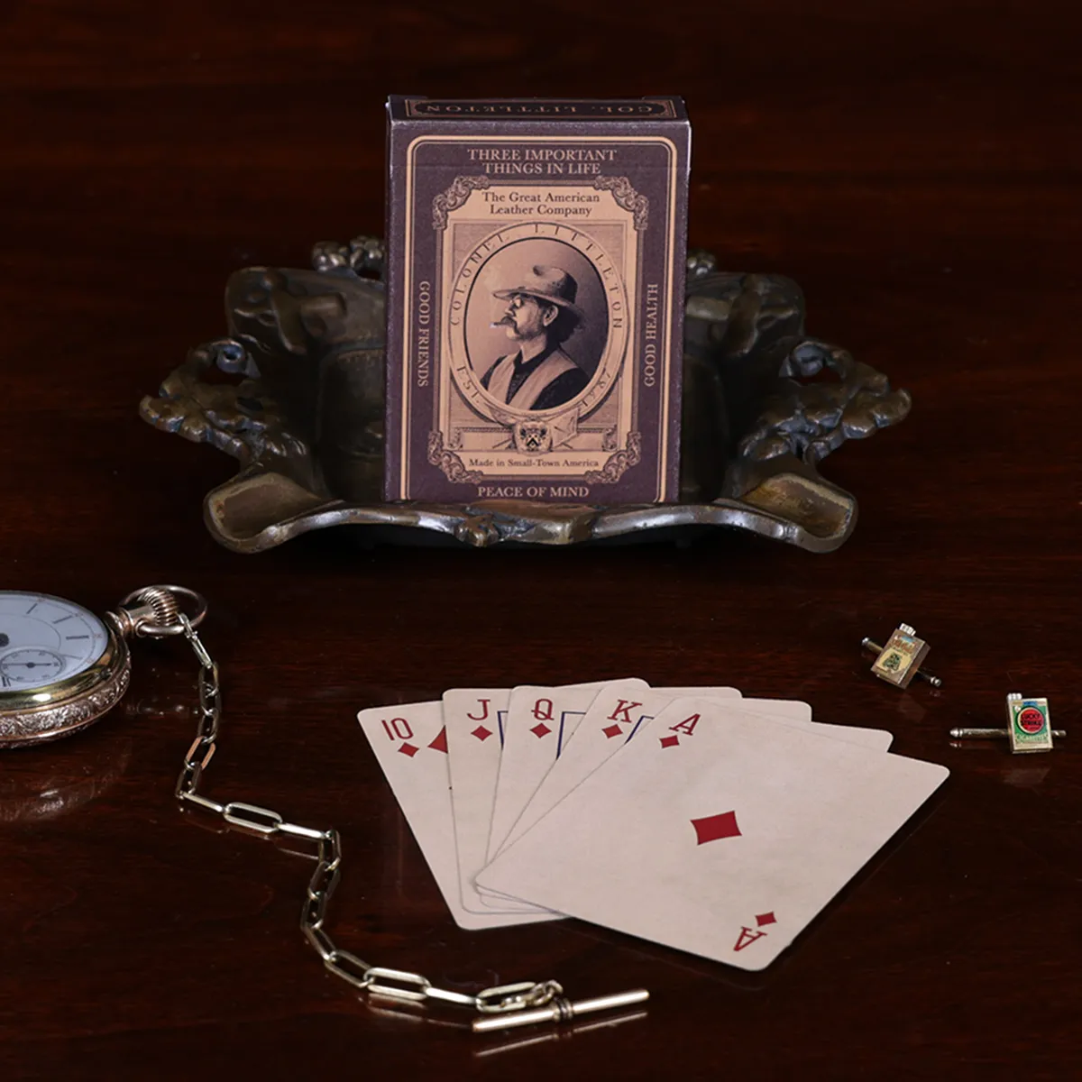 Colonel playing cards box sitting in a vintage cigar ashtray with cards laid out in front with other vintage items surrounding it