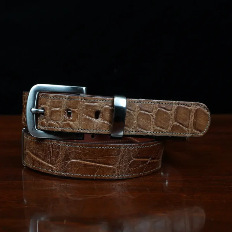 An American Alligator Belt with Nickel hardware showing the front coiled view on a wooden table with black background - id 002