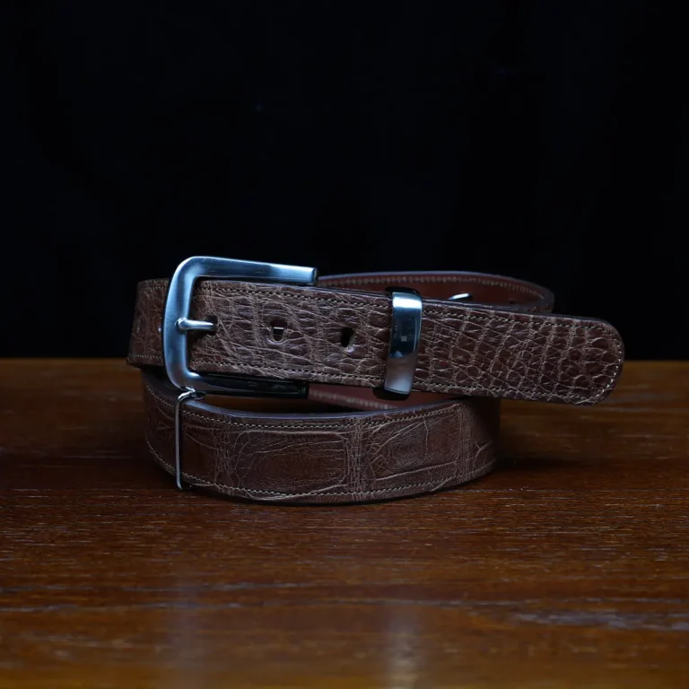 An American Alligator Belt with Nickel hardware showing the front coiled view on a wooden table with black background - id 002
