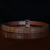 An American Alligator Belt with Nickel hardware showing the back view on a wooden table with black background