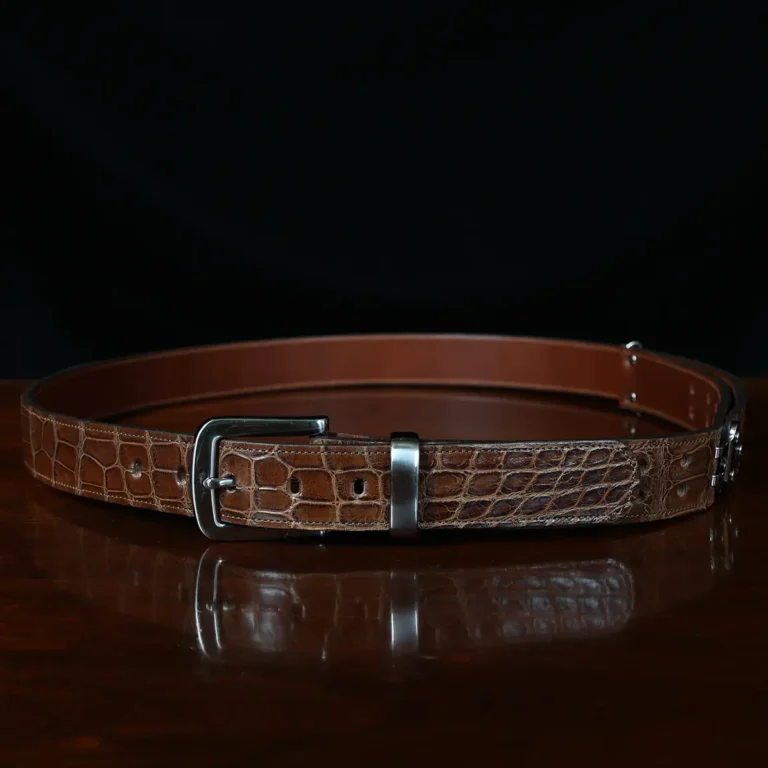 An American Alligator Belt with Nickel hardware showing the front view on a wooden table with black background