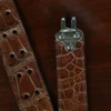 An American Alligator Belt with Nickel hardware showing the clasp view on a wooden table with black background