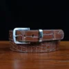 An American Alligator Belt with Nickel hardware showing the front coiled view on a wooden table with black background - id 002