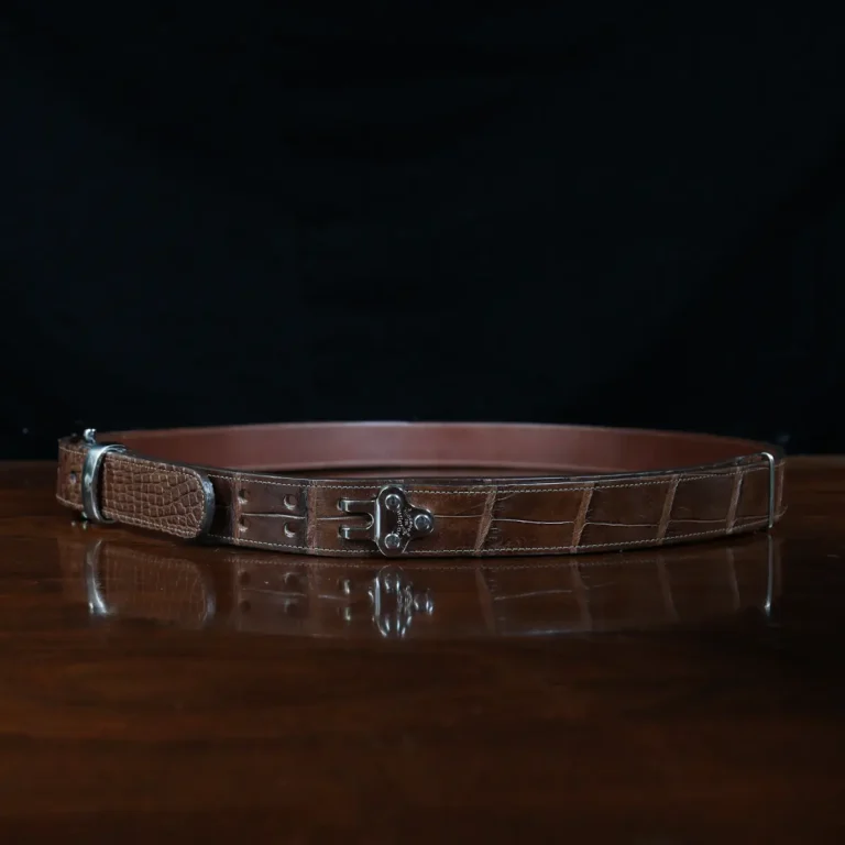 An American Alligator Belt with Nickel hardware showing the side view on a wooden table with black background - id 002