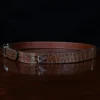 An American Alligator Belt with Nickel hardware showing the side view on a wooden table with black background