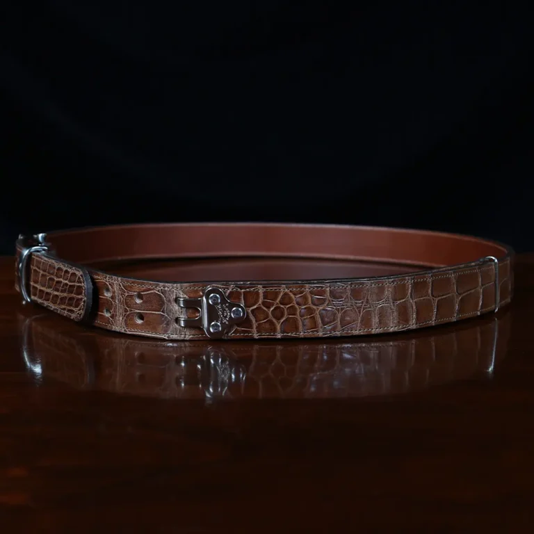 An American Alligator Belt with Nickel hardware showing the side view on a wooden table with black background