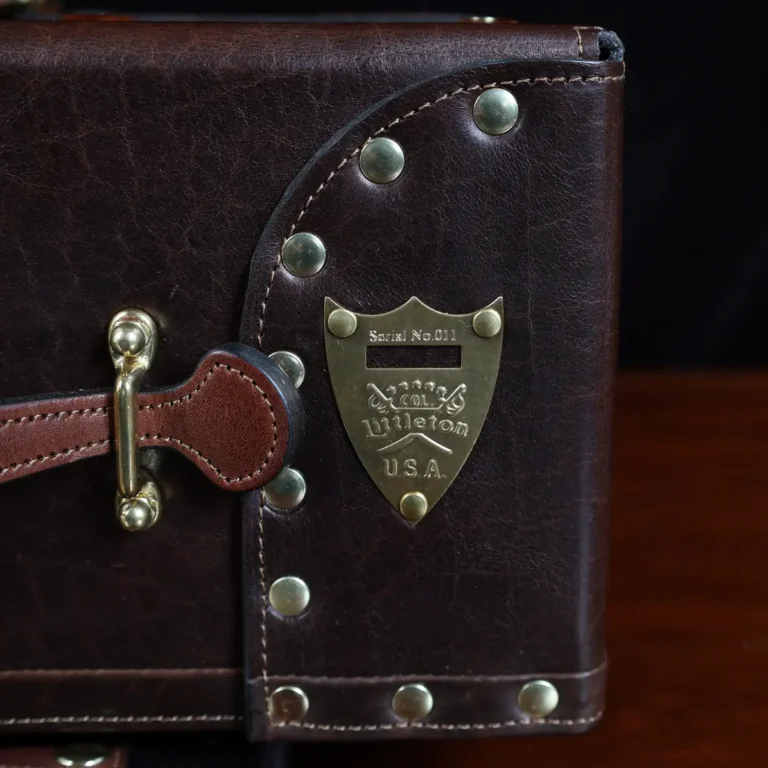 no 3 travel trunk in american buffalo - showing the pommel shield with a dark background on wood table